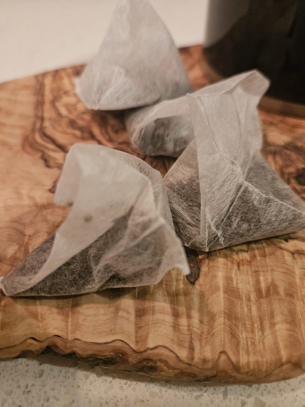 Double Cream of Earl Grey pyramid tea bags on a wooden board beside a dark mug