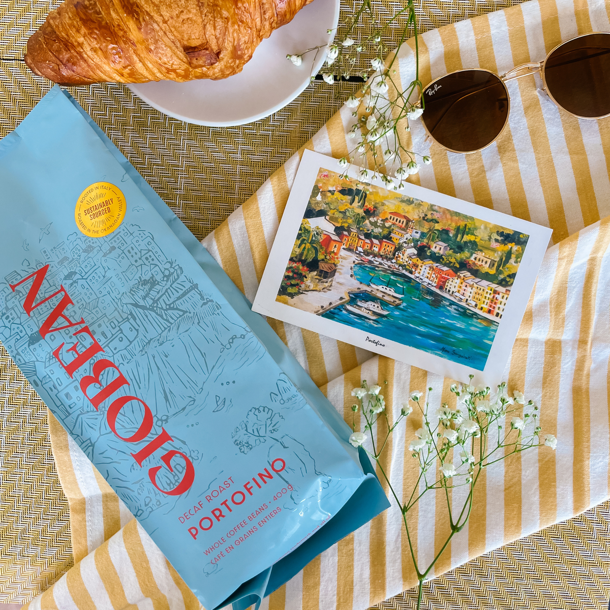 Giobean Portofino decaf coffee bag on a table with a croissant and a postcard